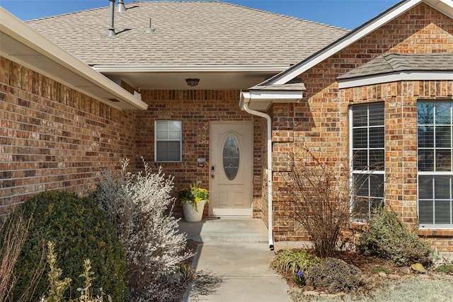 doorway to property featuring brick siding and roof with shingles