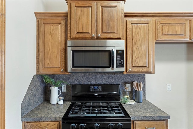 kitchen featuring brown cabinets, stainless steel microwave, dark countertops, black gas stove, and decorative backsplash