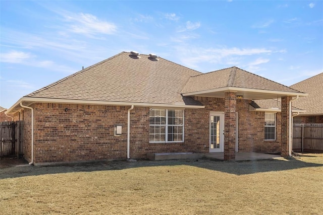 back of property with brick siding, a shingled roof, fence, a yard, and a patio