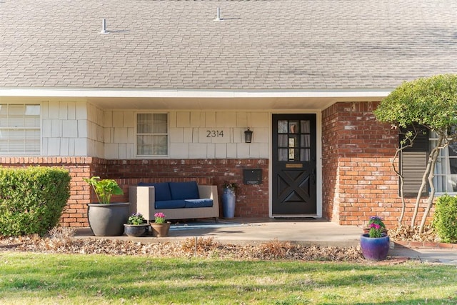 view of exterior entry featuring an outdoor living space, brick siding, and roof with shingles