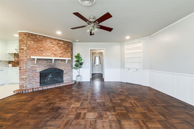 unfurnished living room with a wainscoted wall, a fireplace, crown molding, and visible vents