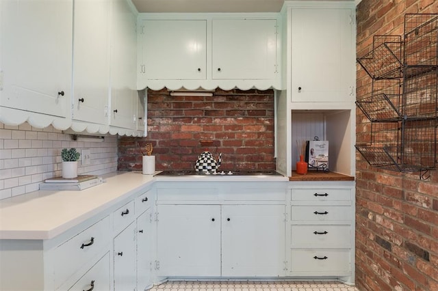 kitchen featuring brick wall, cooktop, light countertops, decorative backsplash, and white cabinets