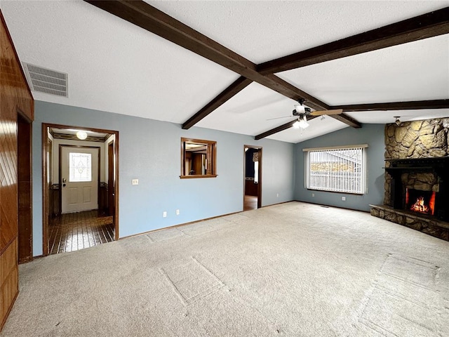 unfurnished living room with visible vents, lofted ceiling with beams, carpet flooring, a stone fireplace, and a textured ceiling