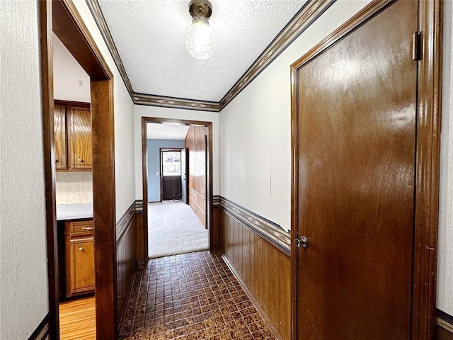 hallway featuring a textured ceiling, wood walls, wainscoting, and crown molding