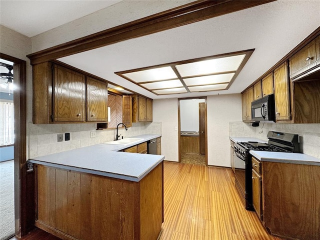 kitchen featuring black appliances, light wood-style flooring, a sink, tasteful backsplash, and a peninsula