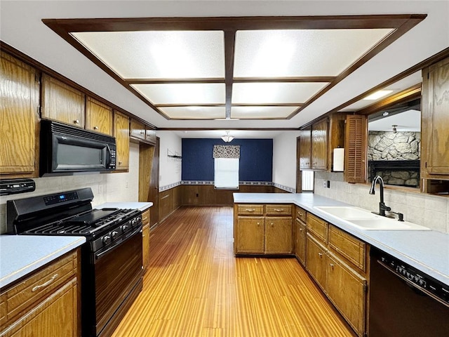 kitchen with a wainscoted wall, light countertops, light wood-style floors, black appliances, and a sink