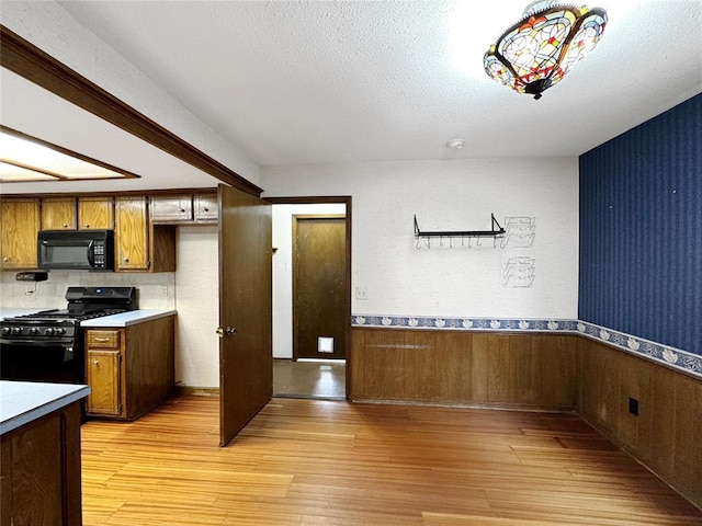 kitchen featuring gas range oven, light wood-style floors, black microwave, and wainscoting