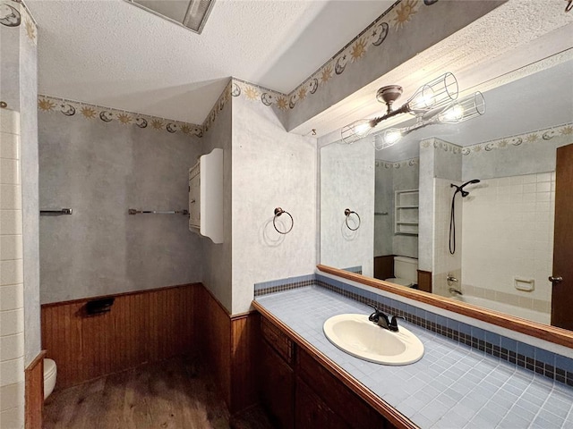 bathroom with toilet, a textured ceiling, wood finished floors, wainscoting, and bathing tub / shower combination