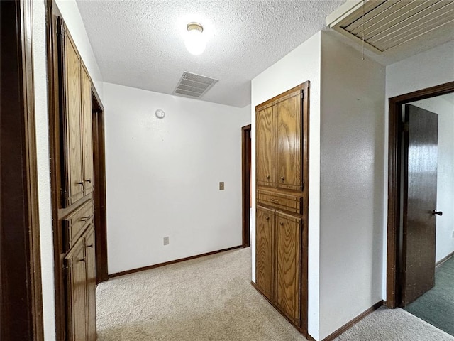 corridor featuring light carpet, visible vents, a textured ceiling, and attic access