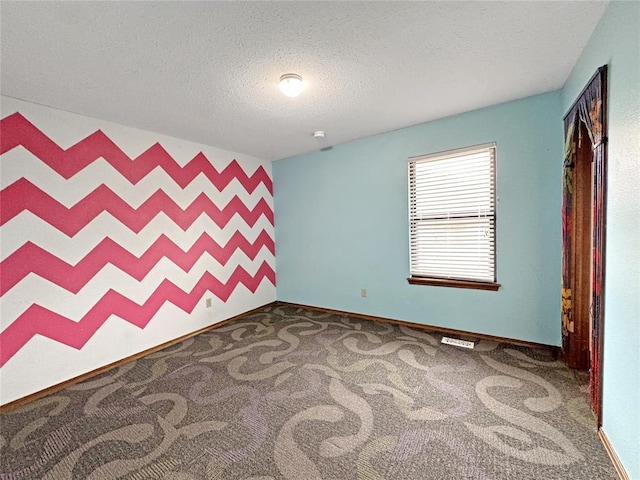 carpeted empty room featuring a textured ceiling, an accent wall, and baseboards