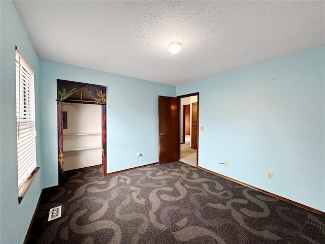 unfurnished bedroom with carpet flooring, multiple windows, a textured ceiling, and baseboards