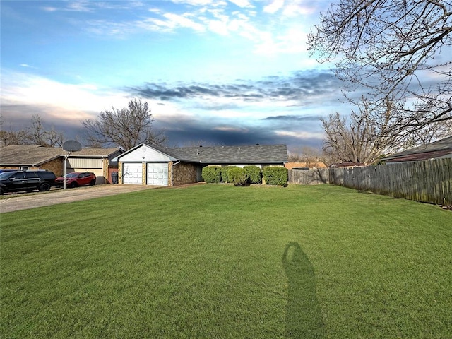 view of yard with an attached garage, driveway, and fence