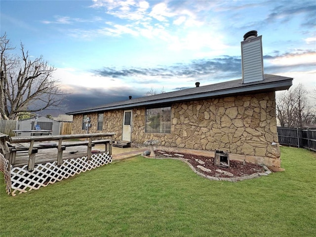 rear view of house featuring a lawn, fence, stone siding, and a wooden deck