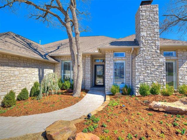 doorway to property featuring a shingled roof, stone siding, and a chimney