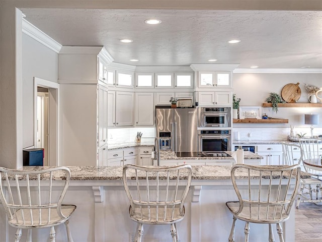 kitchen featuring appliances with stainless steel finishes, a textured ceiling, white cabinetry, crown molding, and a kitchen bar