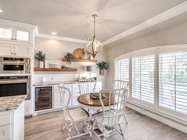 dining area with light wood finished floors, an inviting chandelier, ornamental molding, wine cooler, and a textured ceiling