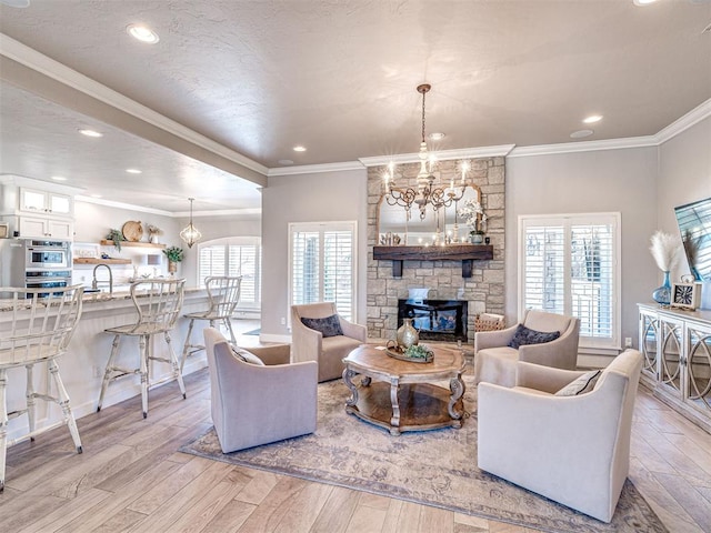 living room with ornamental molding, a textured ceiling, light wood-style floors, an inviting chandelier, and a fireplace