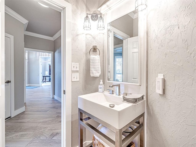 bathroom with vanity, crown molding, a textured wall, and baseboards