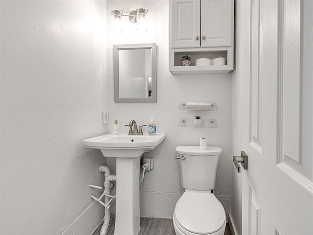 half bath featuring wood finished floors, toilet, and a sink