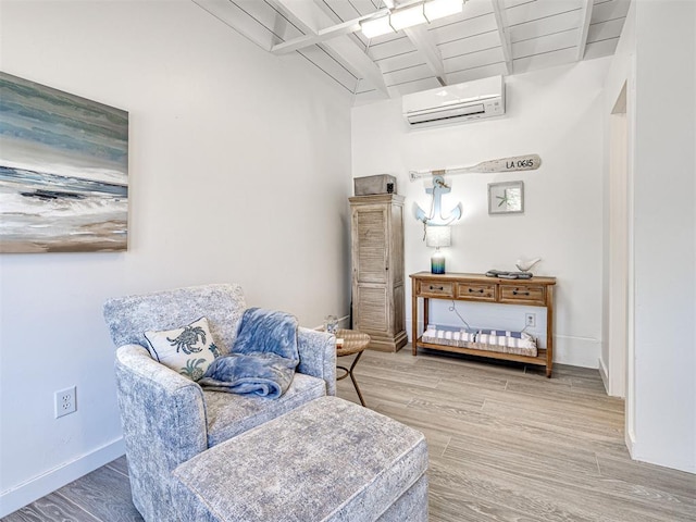 sitting room with beam ceiling, a wall mounted air conditioner, baseboards, and wood finished floors