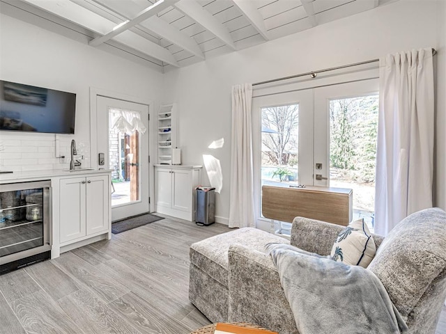 living room with beam ceiling, beverage cooler, french doors, light wood finished floors, and wood ceiling