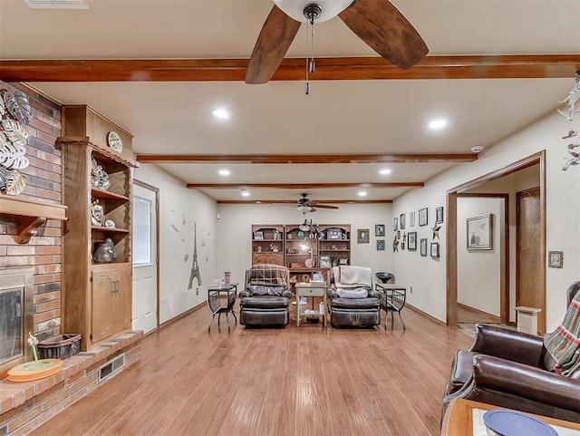 living room with light wood finished floors, ceiling fan, beamed ceiling, recessed lighting, and a fireplace