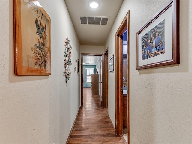 hallway featuring visible vents, a textured wall, and wood finished floors