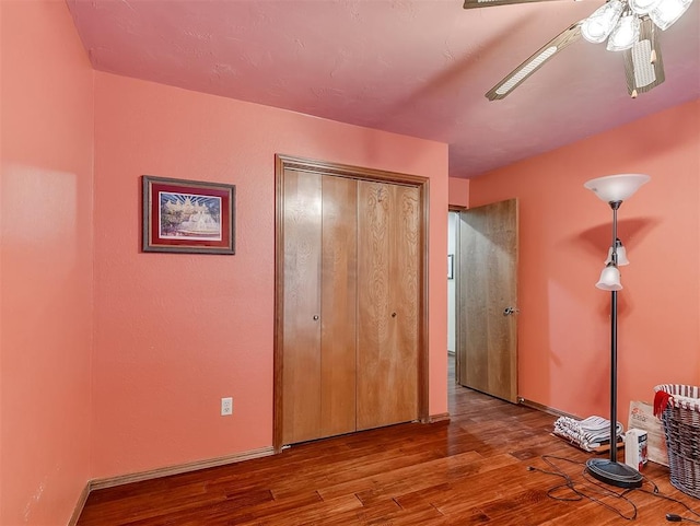 unfurnished bedroom featuring ceiling fan, a closet, baseboards, and wood finished floors