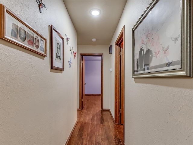 hallway featuring a textured wall, baseboards, and wood finished floors