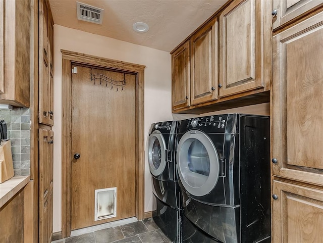 washroom with visible vents, cabinet space, stone finish floor, and washing machine and clothes dryer