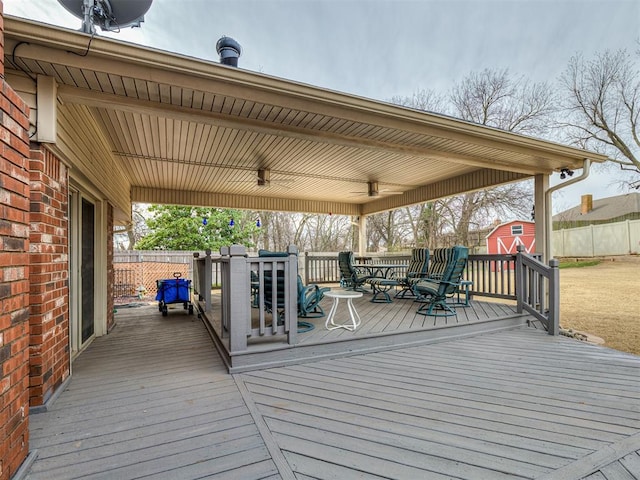 wooden deck featuring outdoor dining area, an outdoor structure, a shed, and fence