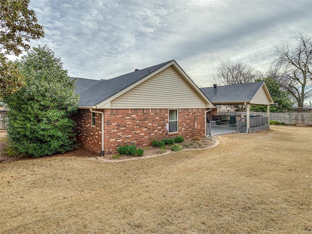 view of side of property featuring brick siding, a shingled roof, a yard, and fence