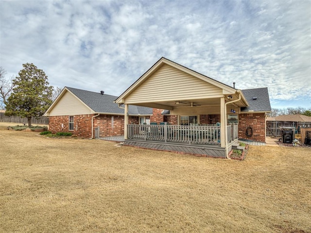 rear view of house with brick siding, a ceiling fan, a yard, and fence