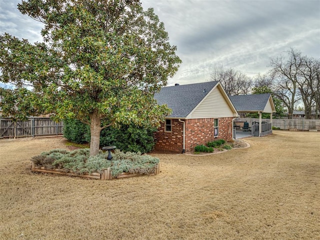 exterior space featuring brick siding, a lawn, a shingled roof, and fence