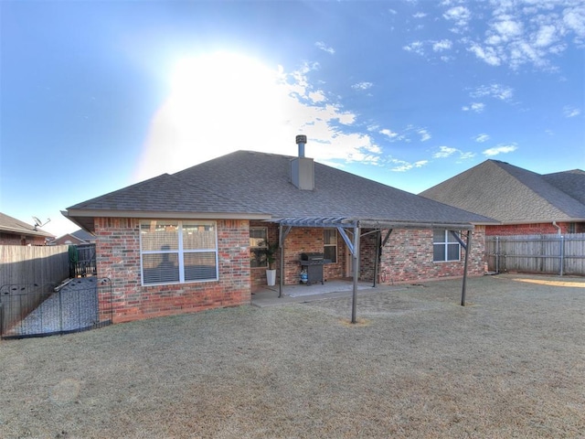 rear view of property with a yard, a fenced backyard, a shingled roof, a patio area, and brick siding