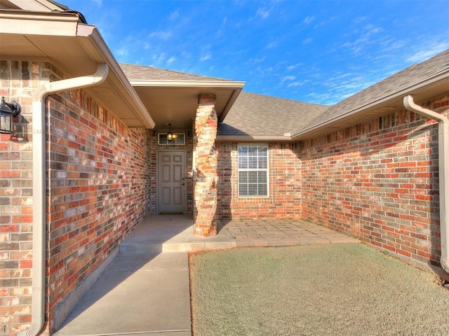 view of exterior entry featuring brick siding and roof with shingles