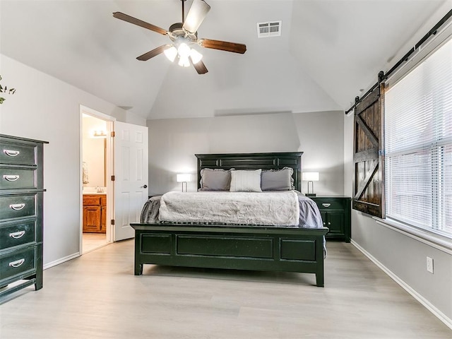 bedroom featuring lofted ceiling, a barn door, visible vents, and light wood finished floors