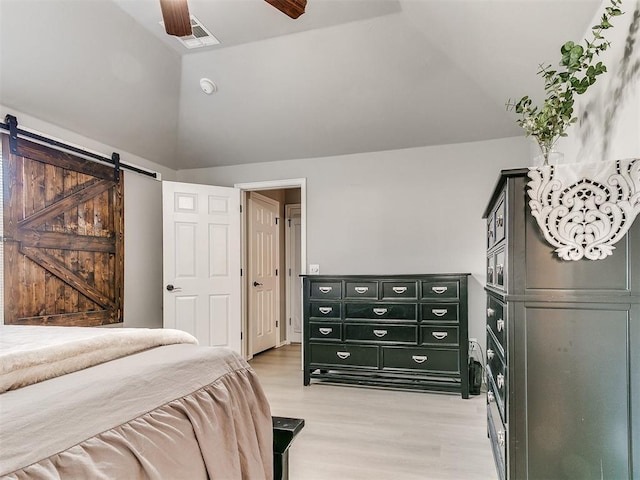 bedroom with light wood finished floors, visible vents, a barn door, lofted ceiling, and a ceiling fan