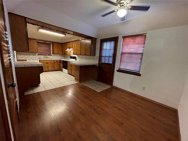 kitchen with white electric range, light wood-style floors, brown cabinetry, decorative backsplash, and tile counters