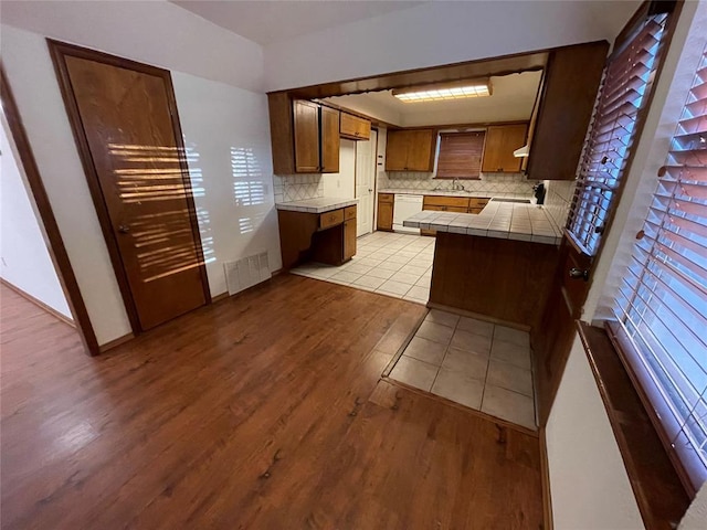 kitchen with tile countertops, visible vents, light wood-style flooring, white dishwasher, and backsplash