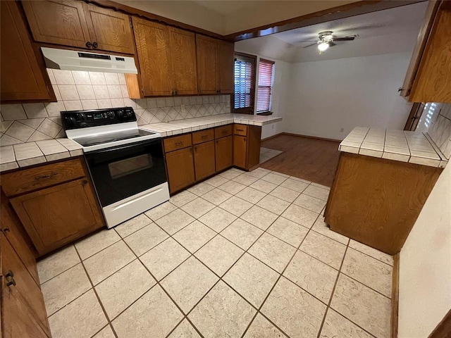 kitchen with under cabinet range hood, tile countertops, and electric range oven