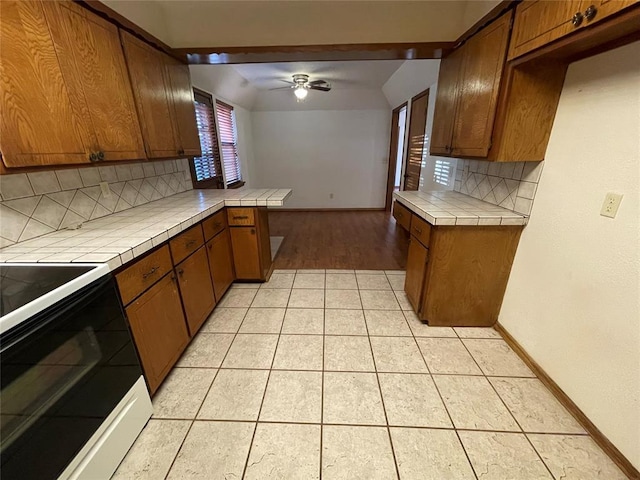 kitchen with light tile patterned flooring, tile countertops, brown cabinets, and a ceiling fan