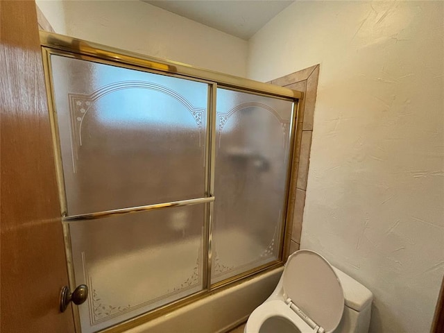 bathroom with toilet, a textured wall, and bath / shower combo with glass door