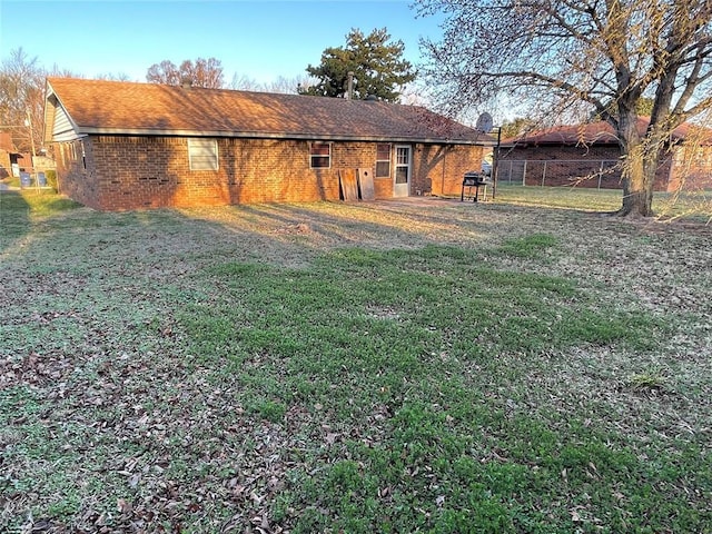 rear view of house featuring brick siding, a shingled roof, a yard, and fence