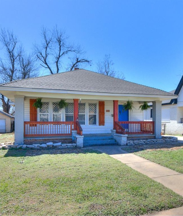 view of front of home featuring brick siding, covered porch, a front yard, and roof with shingles