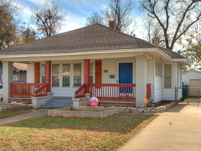 bungalow-style home featuring a chimney, covered porch, driveway, and a shingled roof