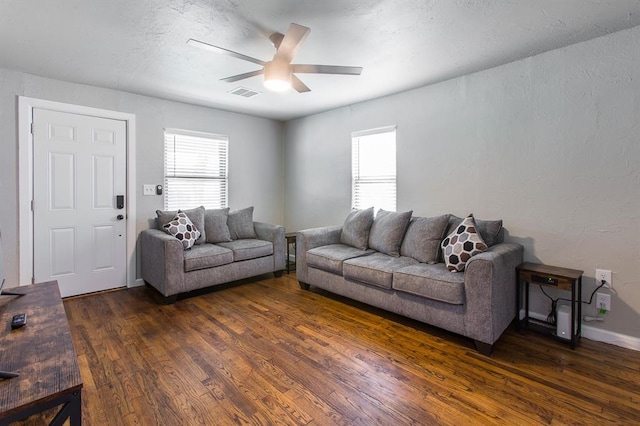 living room featuring a wealth of natural light, visible vents, dark wood-type flooring, and ceiling fan