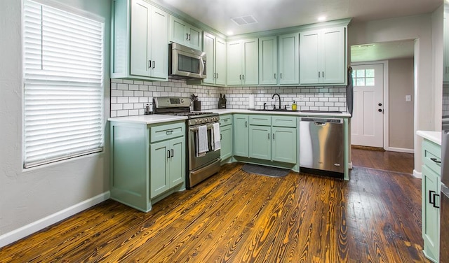 kitchen with dark wood-style flooring, stainless steel appliances, green cabinets, and a sink