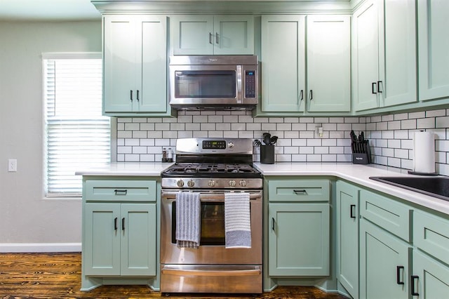 kitchen featuring green cabinets, light countertops, backsplash, and appliances with stainless steel finishes