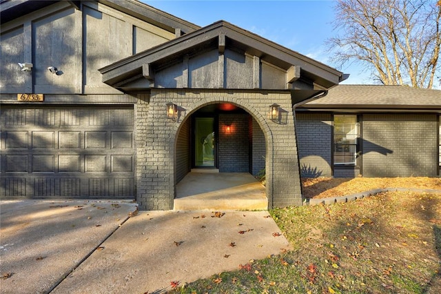 view of exterior entry featuring brick siding, covered porch, driveway, and a garage